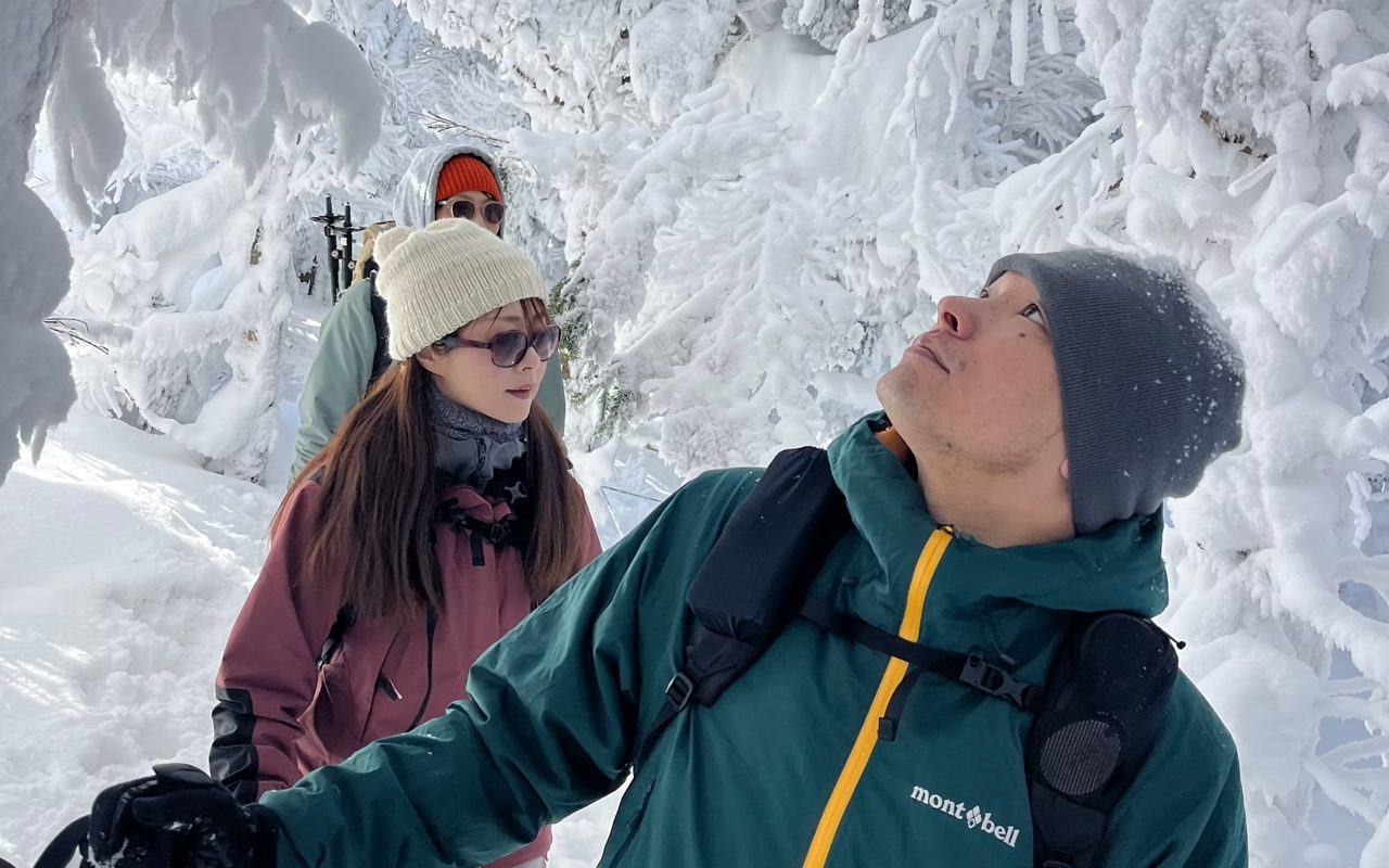 Snowshoers looking up at frost-covered trees in the North Yatsugatake forest