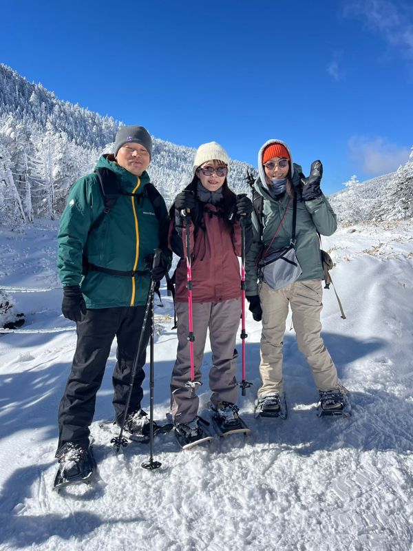 Three guests on snowshoes smiling under a blue sky