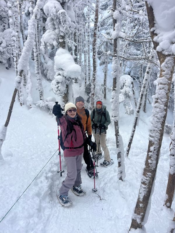 A small group snowshoeing through a frosted birch forest